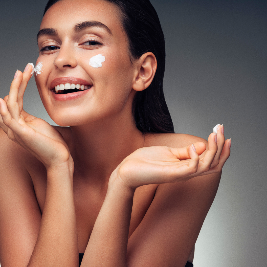 Žena nanosi kremu na lice i smije se – prikaz hidratacije i blistave kože uz HL/Skin kolekciju.