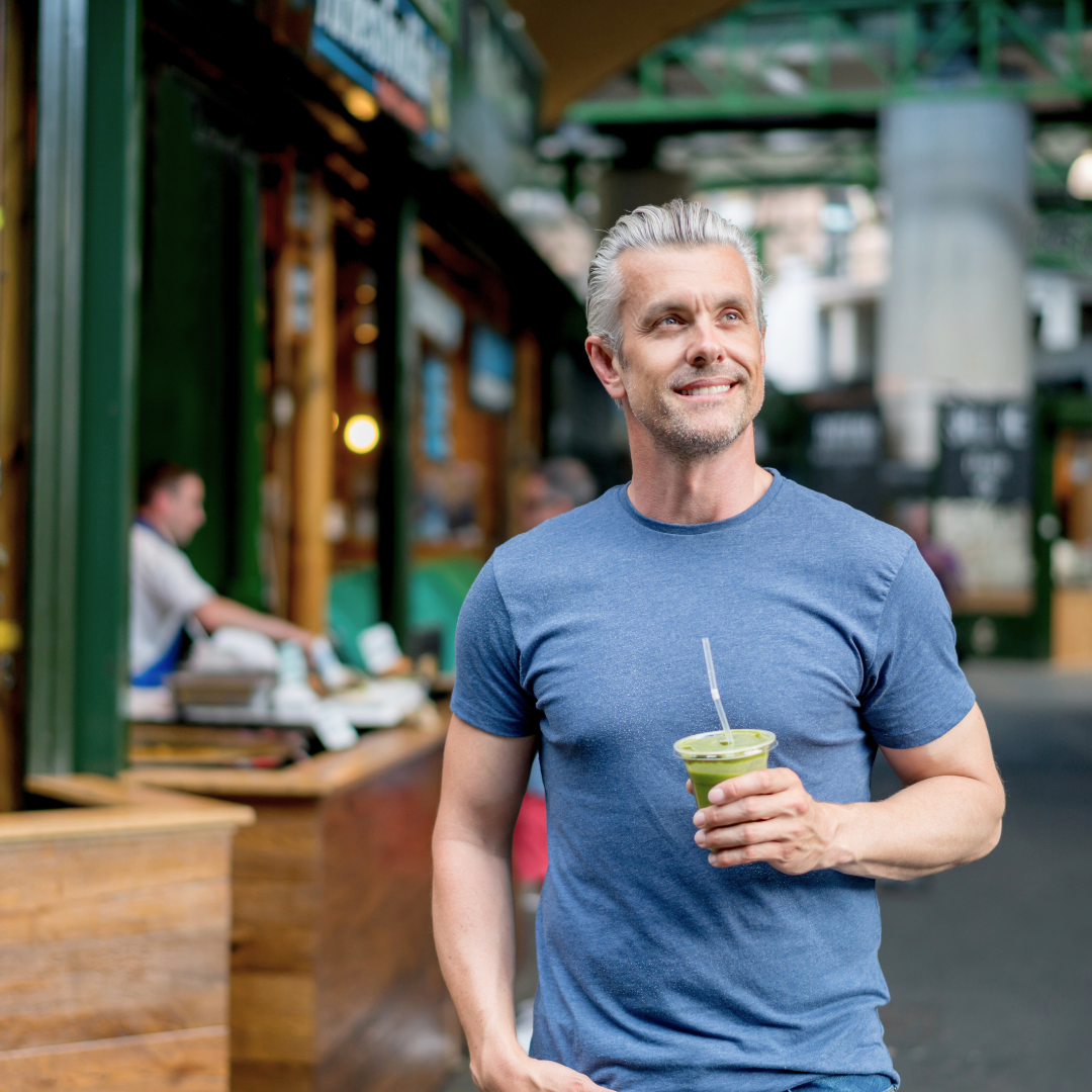 Zdrav i nasmijan muškarac u plavoj majici šeta gradom s čašom zelenog Herbalife shakea, simbolizirajući aktivan životni stil i uravnoteženu prehranu.