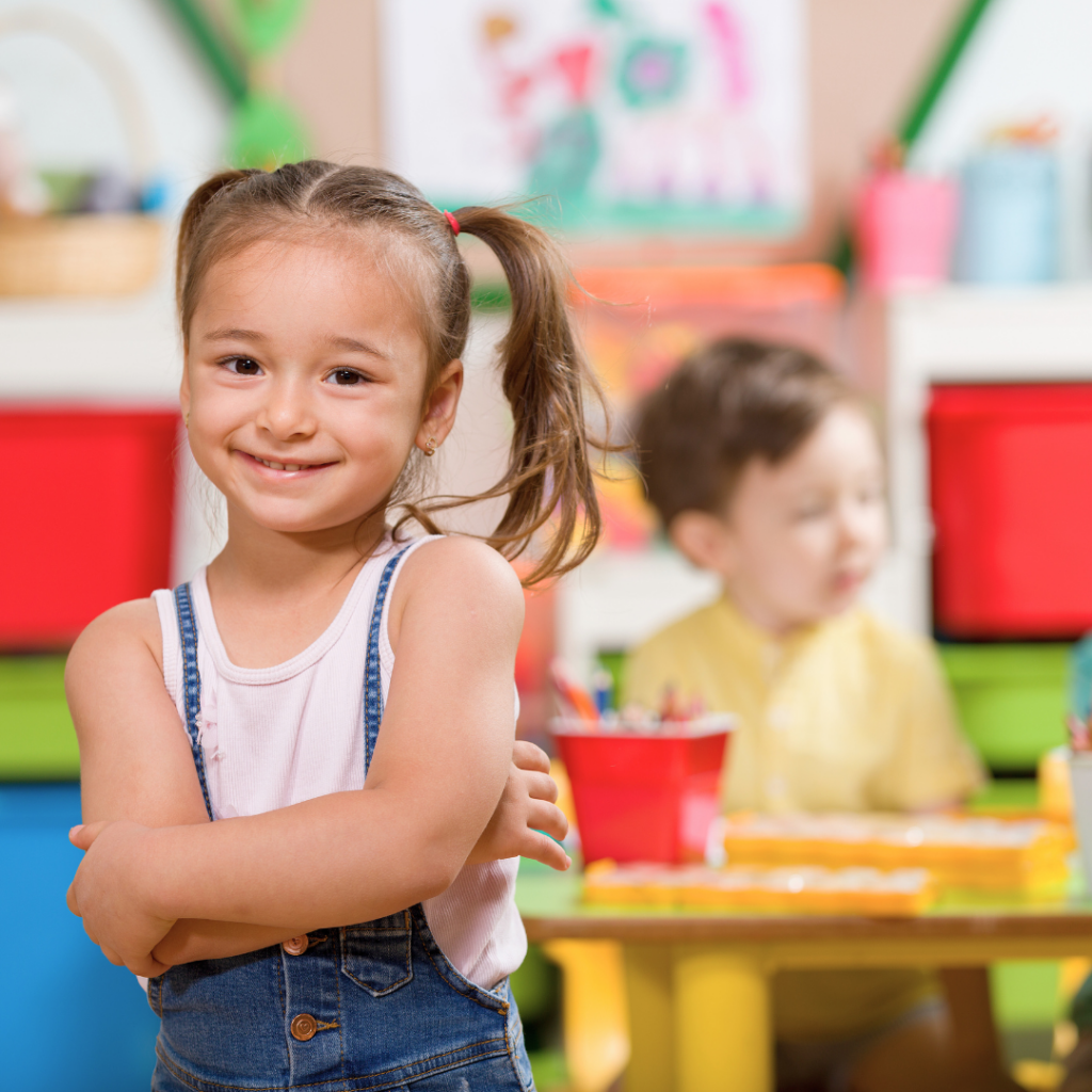 Nasmijana djevojčica u vrtiću s prekriženim rukama, simbol snažnog imuniteta i zdravog razvoja uz podršku dodatka prehrani Forever Kids.