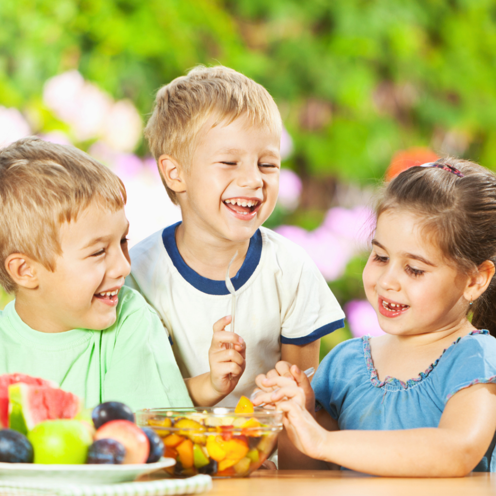 Vesela djeca uživaju u svježem voću na otvorenom, prikaz zdrave prehrane i unosa vitamina uz podršku dodataka poput Forever Kids.