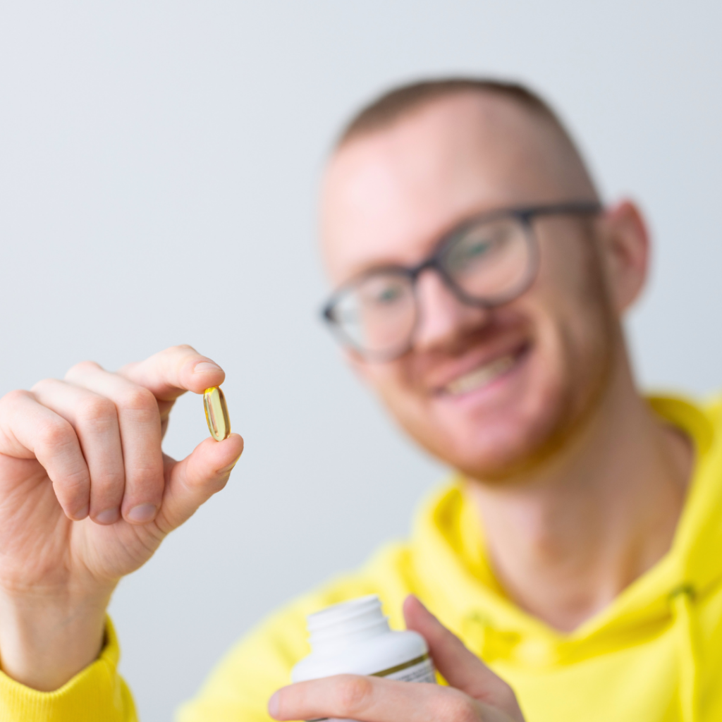 Muškarac u žutoj majici s osmijehom drži kapsulu i bočicu – simbolizira korištenje Forever Living dodataka prehrani za prirodno podizanje razine testosterona.
