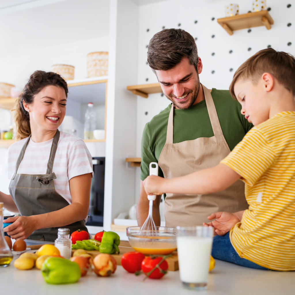 Sretna obitelj u kuhinji zajedno priprema zdrav obrok – roditelji i dijete kuhaju, smiju se i uživaju u zajedničkom vremenu.