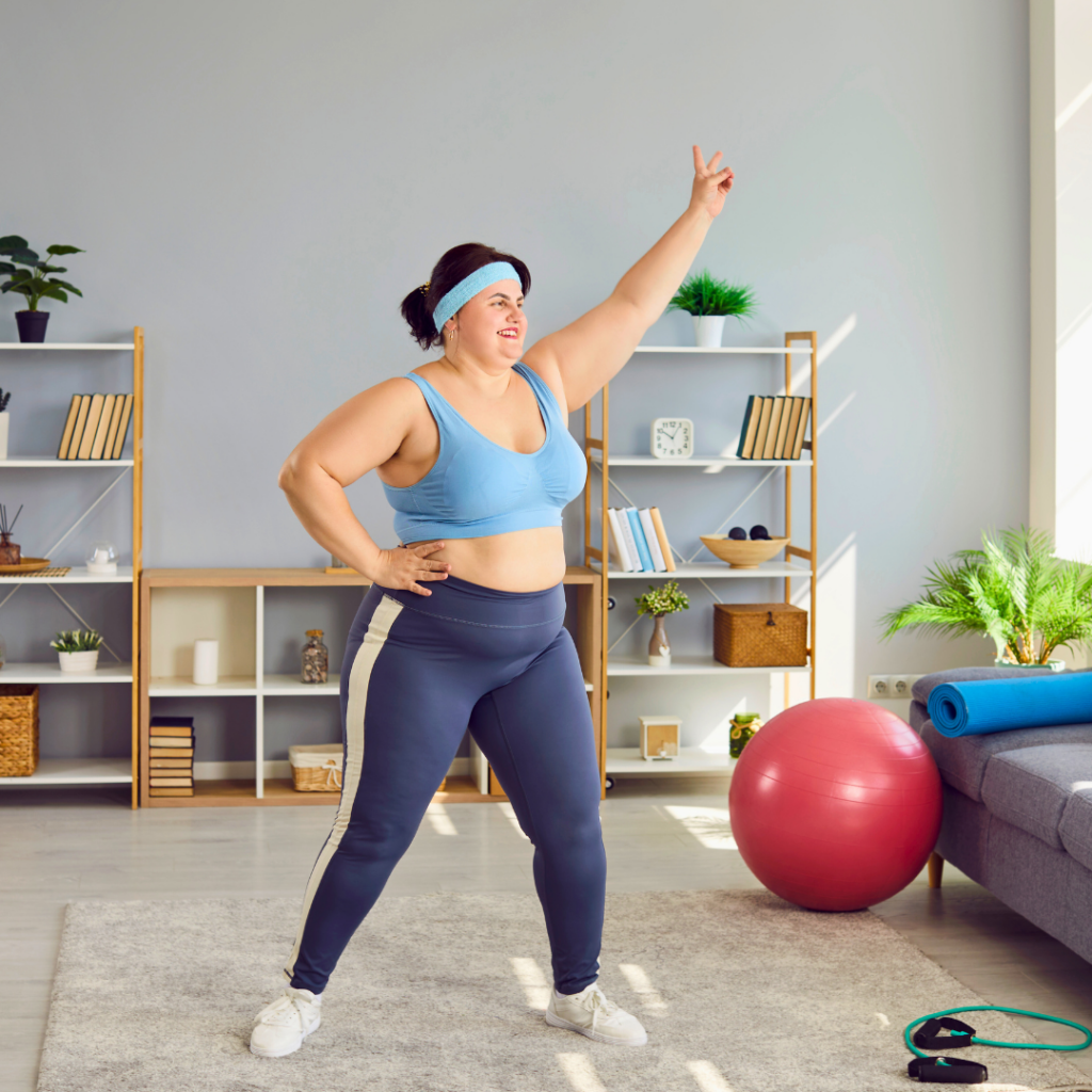 Žena s osmijehom vježba u dnevnoj sobi, odjevena u sportsku odjeću, s rukom podignutom u zrak — motivirana i puna energije tijekom kućnog treninga.