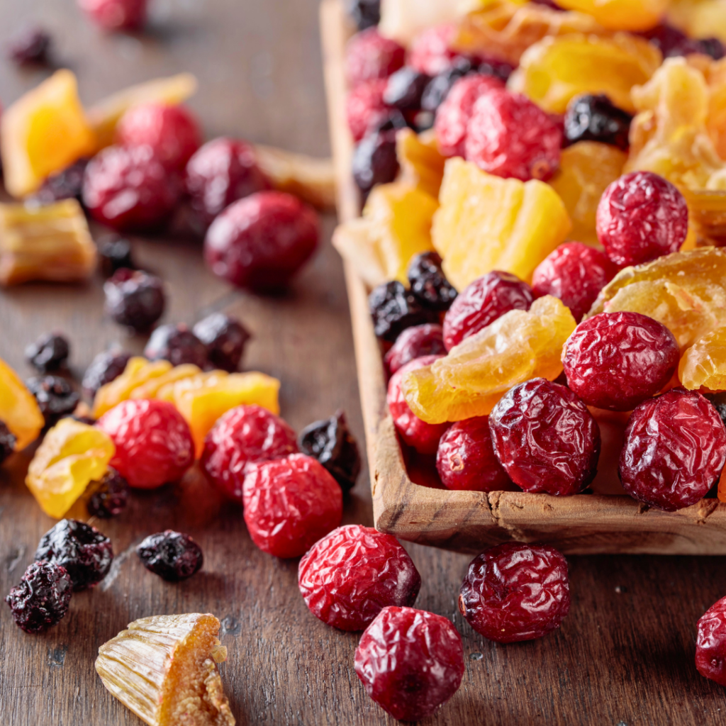 Mješavina sušenog voća poput brusnica, ananasa i grožđica razasuta po drvenoj podlozi, prikazuje zdravu, ali kalorijski bogatu grickalicu.
