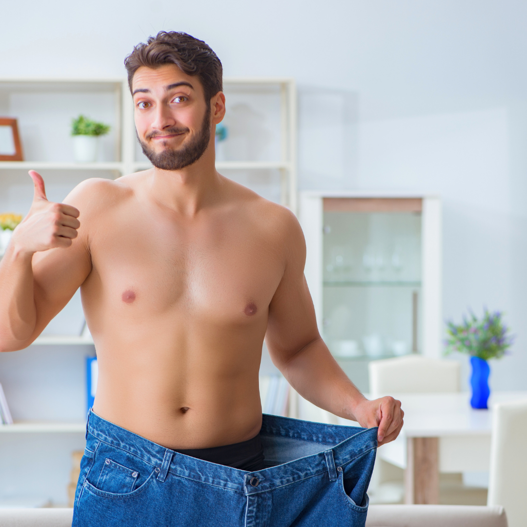Nasmišljen muškarac pokazuje velike traperice nakon uspješnog mršavljenja, simbolizirajući postignute rezultate i zdrav gubitak kilograma.