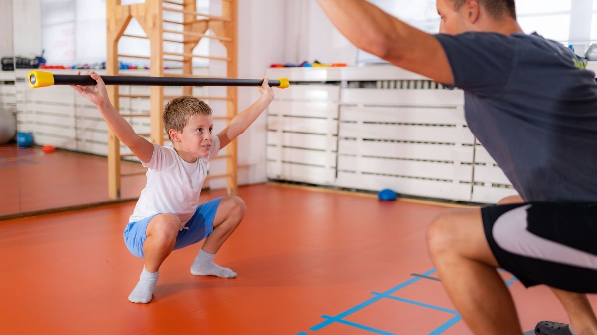 Trening snage za djecu – dječak izvodi čučanj sa šipkom uz stručno vođenje trenera