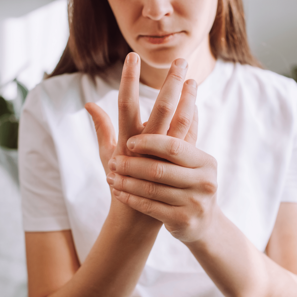 Žena u bijeloj majici drži bolni prst i ruku, pokazujući na nelagodu u zglobovima – čest simptom smanjenog podmazivanja hrskavice. Dodaci prehrani poput Forever Active HA iz Forever Living linije mogu pomoći ublažiti ukočenost i poboljšati funkciju zglobova zahvaljujući hijaluronskoj kiselini niske molekularne mase, uz dodatak kurkume i đumbira.