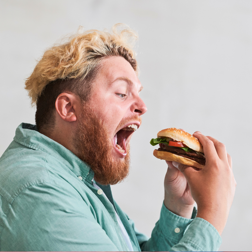 Muškarac jede burger, ilustrirajući kako redovita konzumacija brze hrane može povećati rizik od pretilosti, povišenog kolesterola i metaboličkih poremećaja.